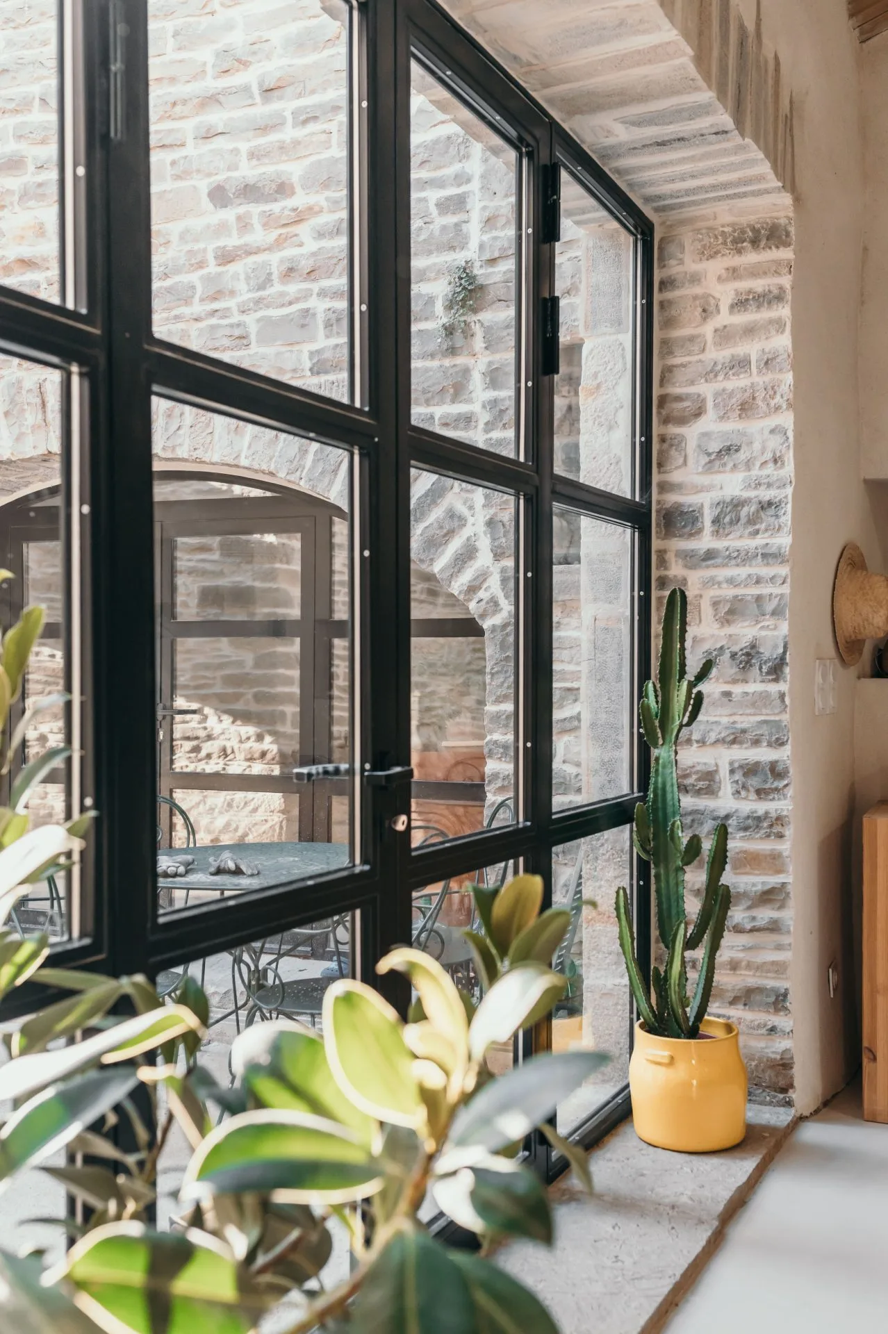 grande-porte-vitree-plantes Chambre aux allures ethniques avec des objets décoratifs artisanaux et du linge de lit en lin. Mélange de teintes terreuses, de blanc et de touches de noir.